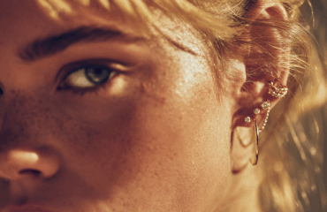 Oreja de mujer joven con un piercing doble hélix, una tendencia de 2024, compuesto por dos aros finos de oro en el cartílago superior.