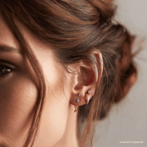 Primer plano de un piercing de oreja tendencia 2025 mostrando un lóbulo apilado con tres pendientes minimalistas de oro.